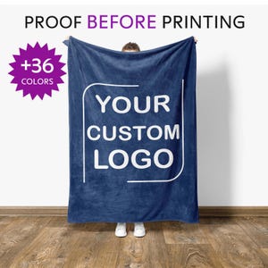 May include: A navy blue blanket with the text "YOUR CUSTOM LOGO" in white. The blanket is held up, with the text "PROOF BEFORE PRINTING" at the top. A purple starburst graphic indicates "+36 COLORS".