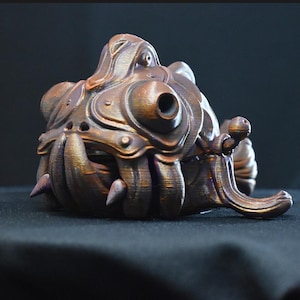 May include: A 3D printed, metallic bronze-colored sculpture of a fantastical creature with a textured, organic design. The creature has a large, round head with a single eye and a small, round mouth. It has a long, thin tail and several appendages.