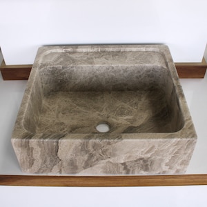 May include: A rectangular, light brown stone sink with a drain hole in the centre. The sink is made of natural stone with a textured surface.