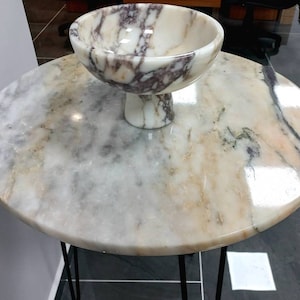 May include: A round marble table with a black metal base and a white marble bowl with purple and brown veins.