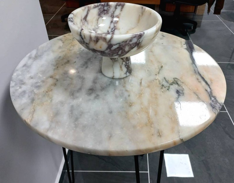 May include: A round marble table with a black metal base and a white marble bowl with purple and brown veins.