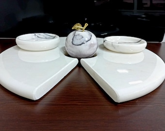 May include: A white marble serving tray with two small bowls and a marble apple sculpture in the center. The tray is divided into two sections, each with a bowl.