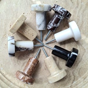 May include: A selection of eight decorative stone knobs in various colours and patterns, including white, black, brown, and beige. Each knob is attached to a silver screw, suitable for furniture or wall decor.