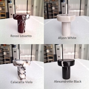 May include: Four marble bottle stoppers in various colours: Rosso Levanto, Afyon White, Calacatta Viola, and Alexandrette Black. Each stopper has a cylindrical stem and a circular top. The colour names are written below each stopper.