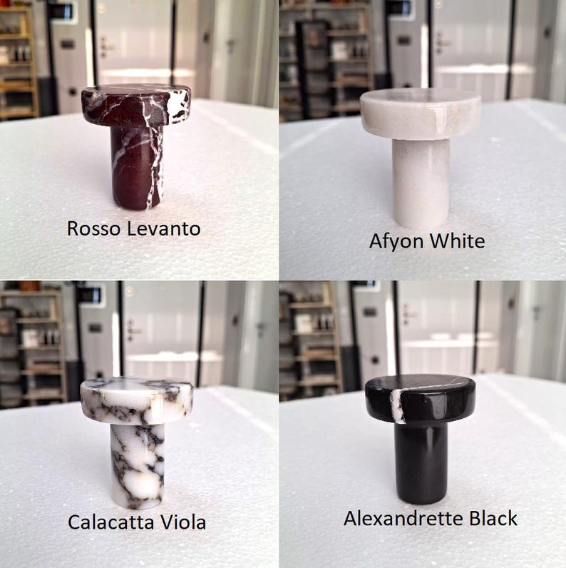 May include: Four marble bottle stoppers in various colours: Rosso Levanto, Afyon White, Calacatta Viola, and Alexandrette Black. Each stopper has a cylindrical stem and a circular top. The colour names are written below each stopper.