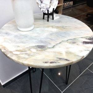 May include: A round marble table with a white and gray veined surface. The table has a black metal hairpin base.