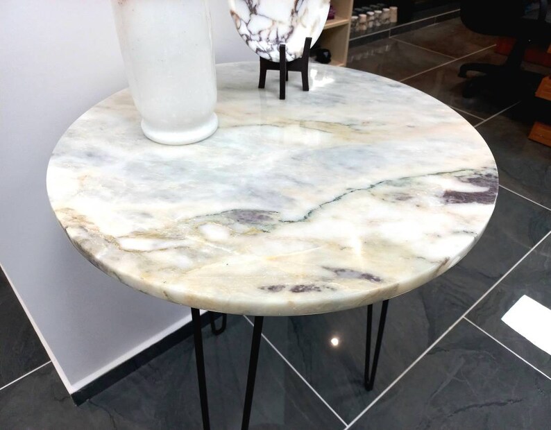 May include: A round marble table with a white and gray veined surface. The table has a black metal hairpin base.