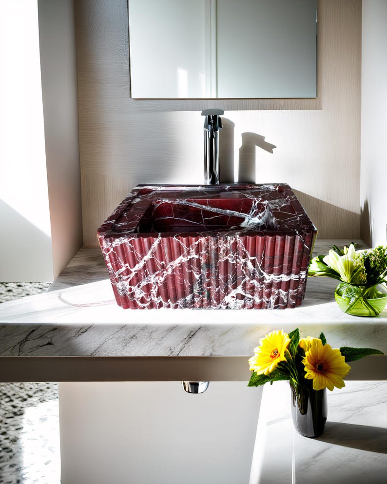 May include: A red marble bathroom sink with white veining, sitting on a white countertop. The sink is rectangular and has a rippled texture. A silver faucet is visible above the sink.