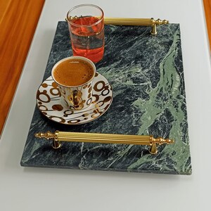 May include: A green marble serving tray with gold handles. The tray has a cup of coffee and a glass of red liquid on it.