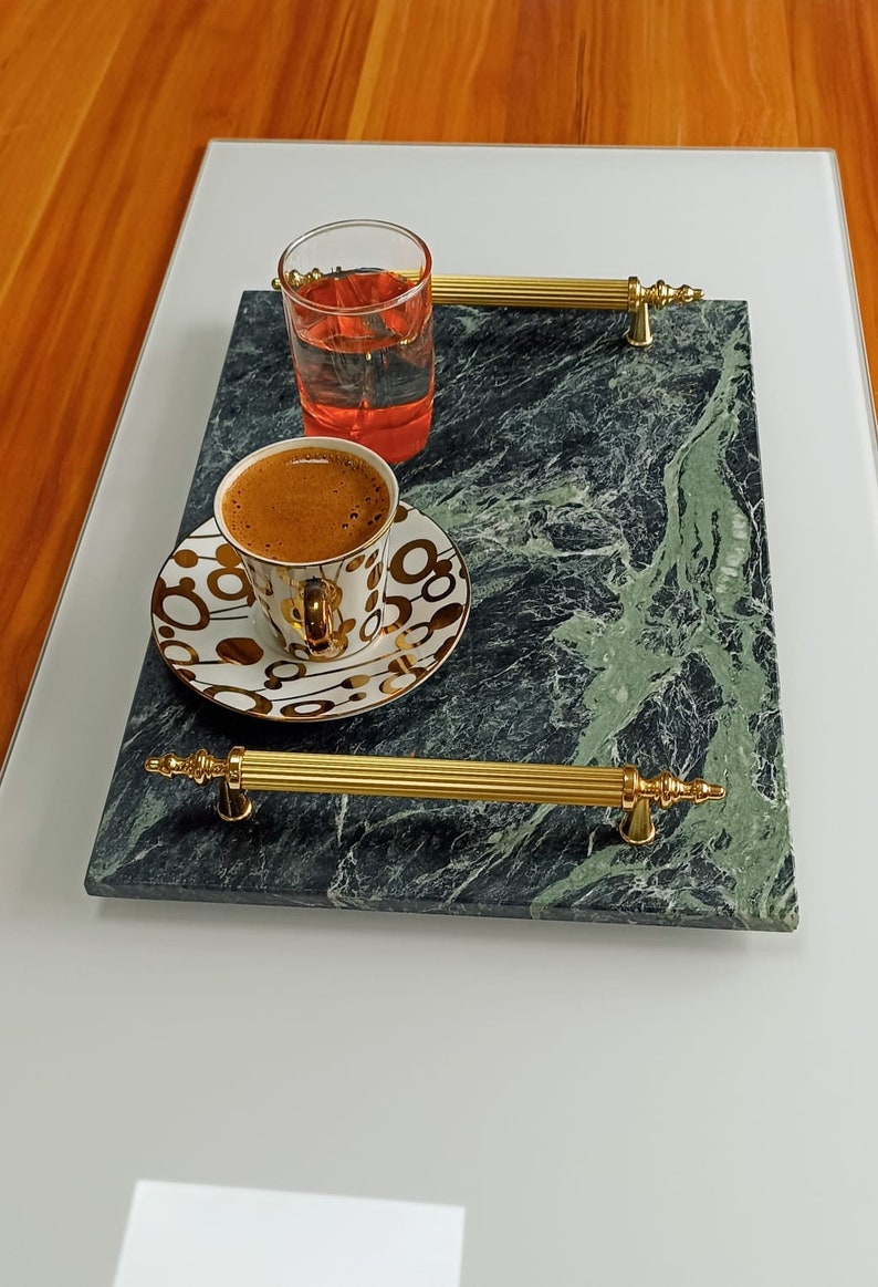 May include: A green marble serving tray with gold handles. The tray has a cup of coffee and a glass of red liquid on it.