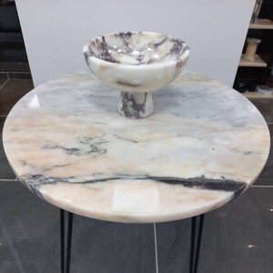 May include: A white marble table with a black metal base and a white marble bowl with purple and grey veins on top.