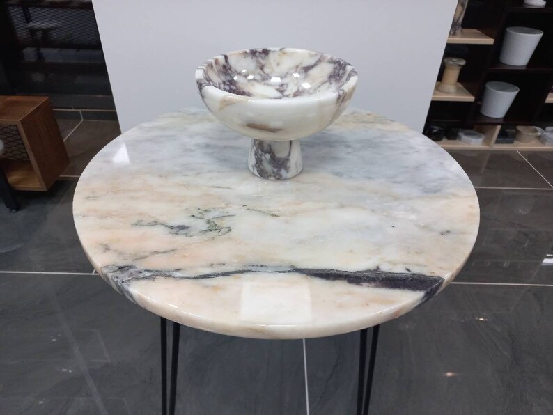 May include: A white marble table with a black metal base and a white marble bowl with purple and grey veins on top.