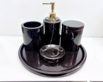 Può includere: Set di accessori per il bagno in marmo nero con un dispenser di sapone, un porta spazzolino da denti e una piccola ciotola. Il set è su un vassoio in marmo nero.