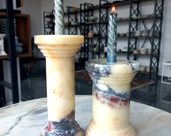 May include: Two marble candle holders with blue and white spiral candles. The candle holders are made of white marble with pink and gray streaks.