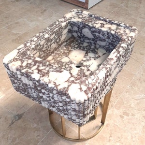 May include: A white and purple marble sink with a fluted edge, sitting on a gold metal stand.
