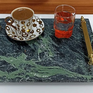 May include: A green marble serving tray with gold handles. The tray has a cup of coffee and a glass of red liquid on it.