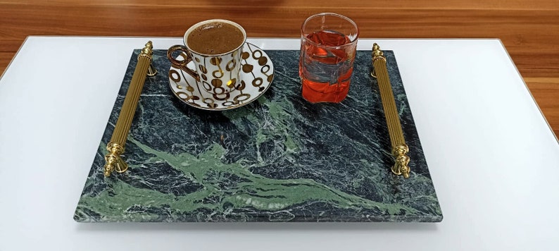 May include: A green marble serving tray with gold handles. The tray has a cup of coffee and a glass of red liquid on it.