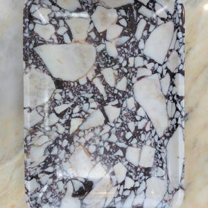 May include: Rectangular serving tray with a glossy finish. The tray features a striking pattern of white and dark purple marble-like fragments set against a dark background. The tray's edges are rounded.