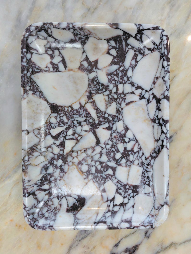 May include: Rectangular serving tray with a glossy finish. The tray features a striking pattern of white and dark purple marble-like fragments set against a dark background. The tray's edges are rounded.