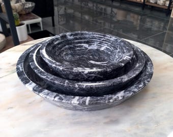 May include: Three black and white marble bowls, nested together, with a white marble background.