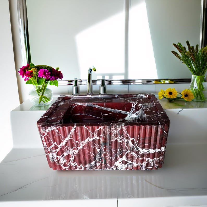 May include: A red and white marble bathroom sink with a rectangular shape and a rippled design. The sink is sitting on a white countertop.