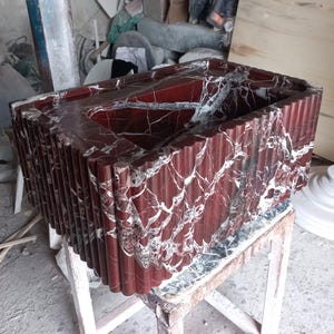 May include: A red marble sink with a rippled edge. The sink is made of a natural stone with white veins.