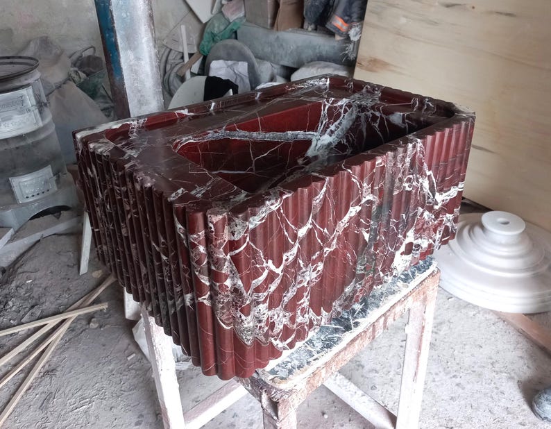 May include: A red marble sink with a rippled edge. The sink is made of a natural stone with white veins.