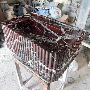 May include: A red and white marble sink with a fluted design. The sink is sitting on a wooden stool.