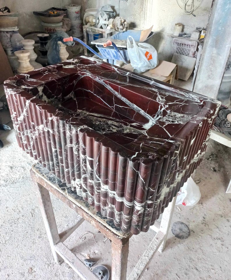 May include: A red and white marble sink with a fluted design. The sink is sitting on a wooden stool.