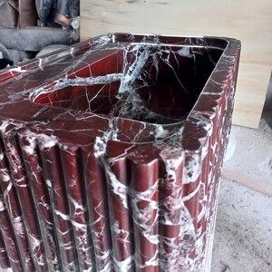 May include: A red marble sink with white veining. The sink is rectangular and has a fluted design on the outside.