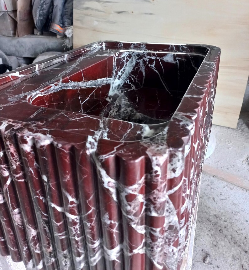 May include: A red marble sink with white veining. The sink is rectangular and has a fluted design on the outside.