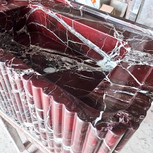 May include: A red marble sink with white veining. The sink is set into a red marble countertop with a fluted edge.