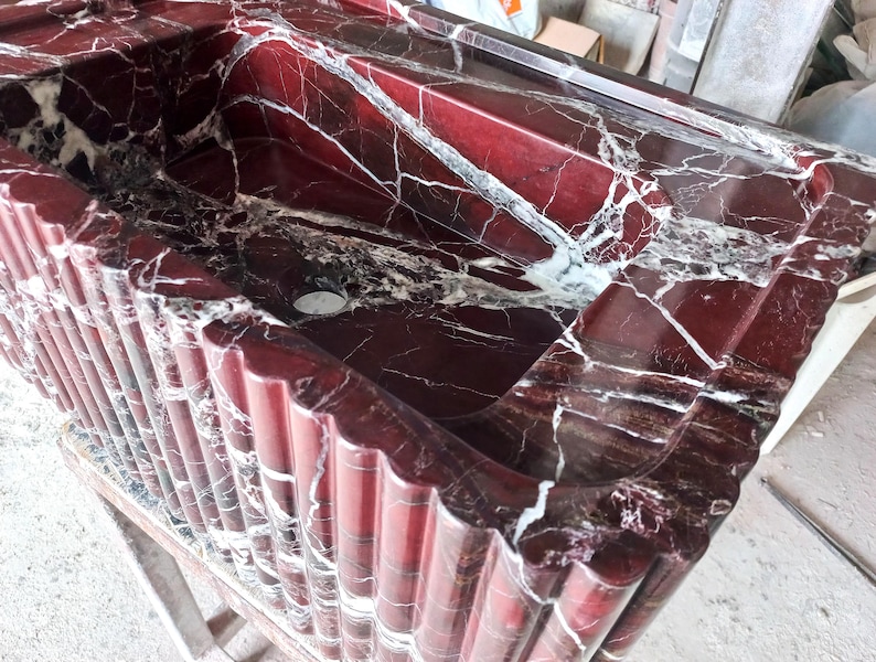 May include: A red marble sink with white veining. The sink is set into a red marble countertop with a fluted edge.