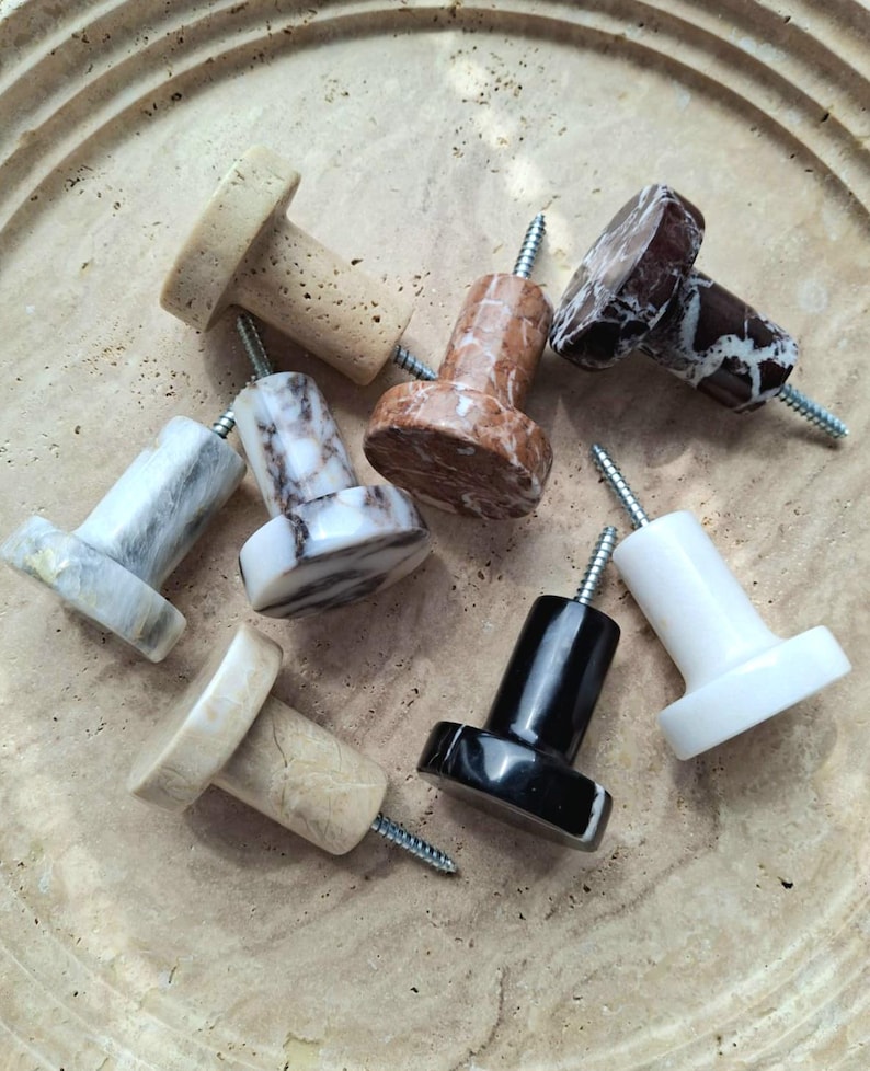 May include: A selection of stone knobs in diverse colours and patterns, such as beige, brown, black, white, and marble. Each knob features a cylindrical base and a screw for simple installation. These knobs are suitable for cabinets and drawers.
