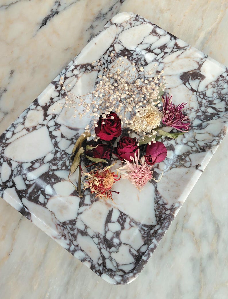 May include: A rectangular marble tray with a white and dark gray pattern, holding dried flowers. The flowers include deep red roses, small white blooms, and various dried flower heads in shades of pink and orange.
