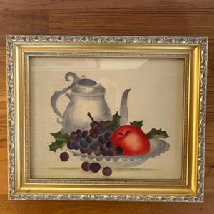 Original theorem painting, 12.5x10 inches framed size, of a still life with teapot, grapes and an apple. Signed on reverse.