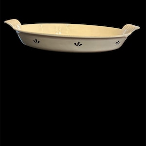 Puede incluir: Fuente ovalada de color crema con dos asas y un estampado floral negro. La fuente tiene una forma ligeramente curvada y está hecha de cerámica. Las asas tienen un diseño acanalado.