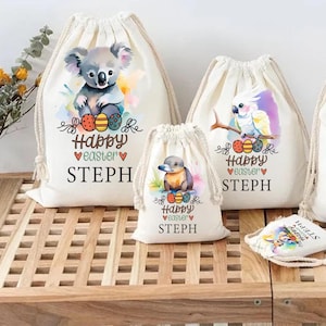 May include: Three white drawstring bags with colourful Easter-themed designs. The bags feature a koala, a cockatoo, and a platypus. Each bag has the text "Happy Easter" and a name, "STEPH".