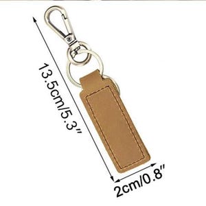 May include: A brown leather keychain with a silver-colored clasp and key rings. The keychain is 5.3 inches long and 0.8 inches wide. The leather has a stitched border. The background is white.