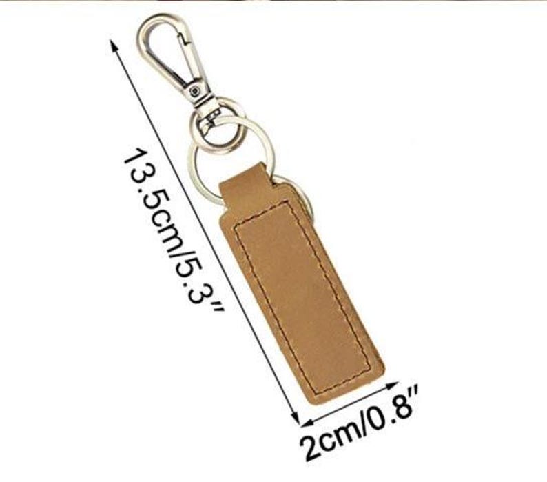May include: A brown leather keychain with a silver-colored clasp and key rings. The keychain is 5.3 inches long and 0.8 inches wide. The leather has a stitched border. The background is white.