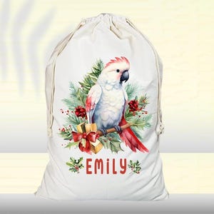 May include: White canvas Christmas gift bag featuring a red and white cockatoo perched on a branch with red berries and a gold gift box. The bag is personalised with the name "Emily".