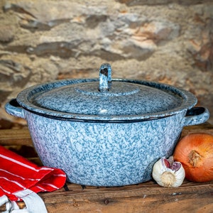Könnte beinhalten: Ein vintage Emailletopf in blau und weiß mit Flecken, mit Deckel und zwei Griffen. Der Topf steht auf einer Holzoberfläche mit einem rot-weiß gestreiften Küchentuch, einer Knoblauchzehe und einer braunen Zwiebel.