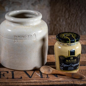 Può includere: Un barattolo di ceramica bianca con la parola "AMORA" stampata sul davanti, accanto a un barattolo di vetro di senape Maille Dijon Original con un coperchio nero e un'etichetta dorata. I barattoli sono su una superficie di legno.