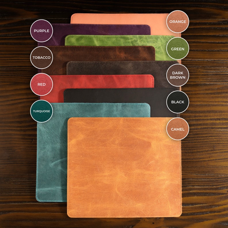May include: A set of eight leather mouse mats in different colours, including orange, green, dark brown, black, camel, turquoise, red, tobacco, and purple. The mouse mats are arranged in a stack, with the orange mouse mat on top and the purple mouse mat on the bottom.