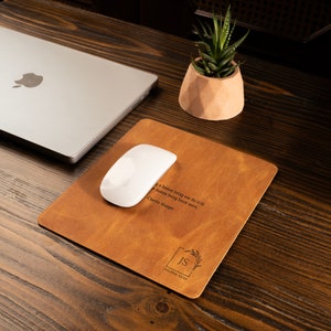 May include: A brown leather desk mat with a quote by Charlie Munger: "The most important thing a human being can do is to know more." The mat also has a monogram with the initials "IS" and the name "JULIANA SILVA" engraved on it.