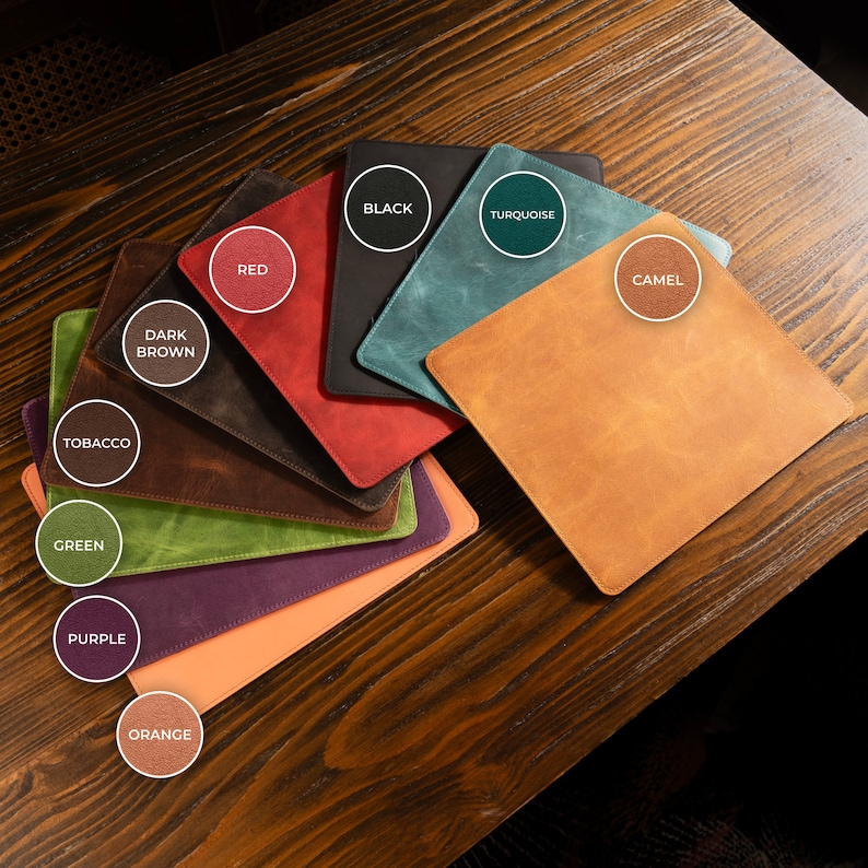 May include: A selection of leather mouse mats in various colours, including black, turquoise, camel, red, dark brown, tobacco, green, purple, and orange. Each mat features a circle with the colour name written inside.