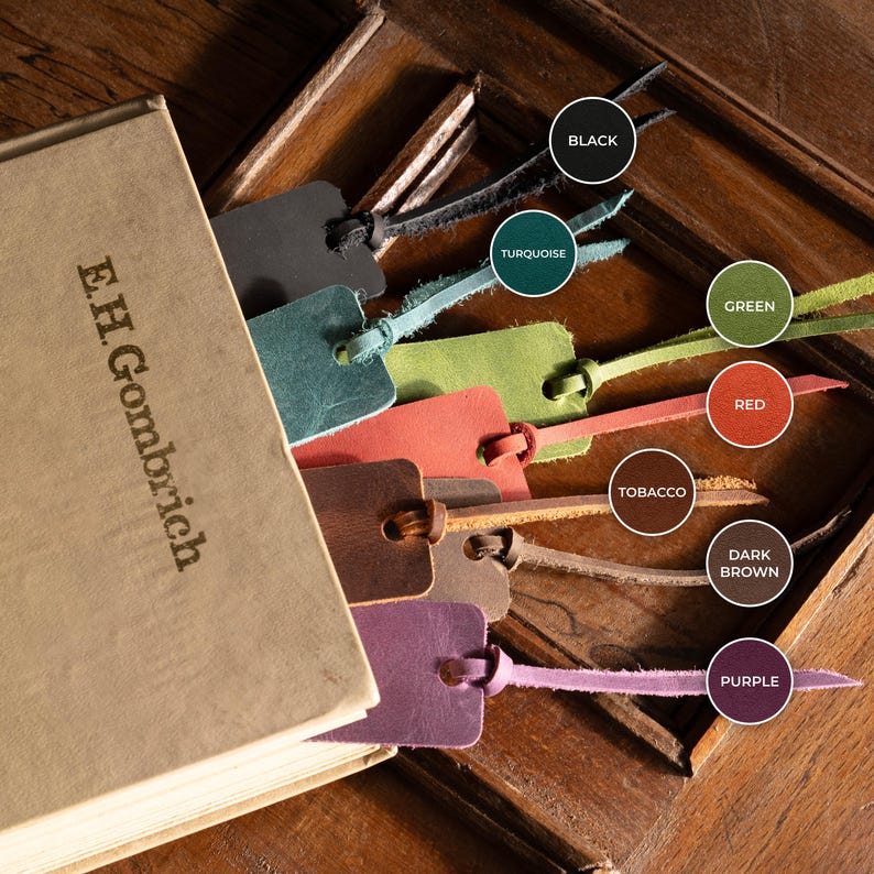 K&ouml;nnte beinhalten: Ein Buch mit dem Text "E.H. Gombrich" und mehrere Leder-Lesezeichen in verschiedenen Farben, darunter Schwarz, T&uuml;rkis, Gr&uuml;n, Rot, Tabak, Dunkelbraun und Lila. Die Lesezeichen sind in das Buch eingelegt und zeigen ihre unterschiedlichen Farbt&ouml;ne.
