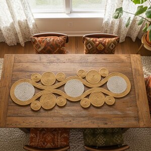 Peut inclure: Vue aérienne d'une table à manger en bois avec un chemin de table en jute tressé. Quatre chaises avec des coussins à motifs entourent la table. Un tapis blanc et une plante en pot sont également visibles.