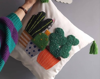 May include: White pillow with green, orange, and yellow embroidered cacti in pots. The pillow has green tassels on the corners.