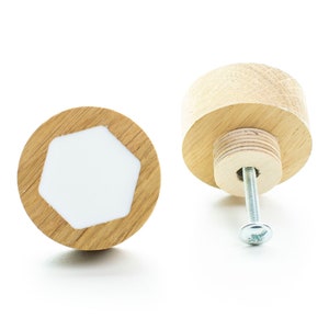 Puede incluir: Dos pomos de armario de madera con una incrustación hexagonal blanca. Un pomo se muestra de lado con un tornillo sujeto. El otro pomo se muestra de frente.
